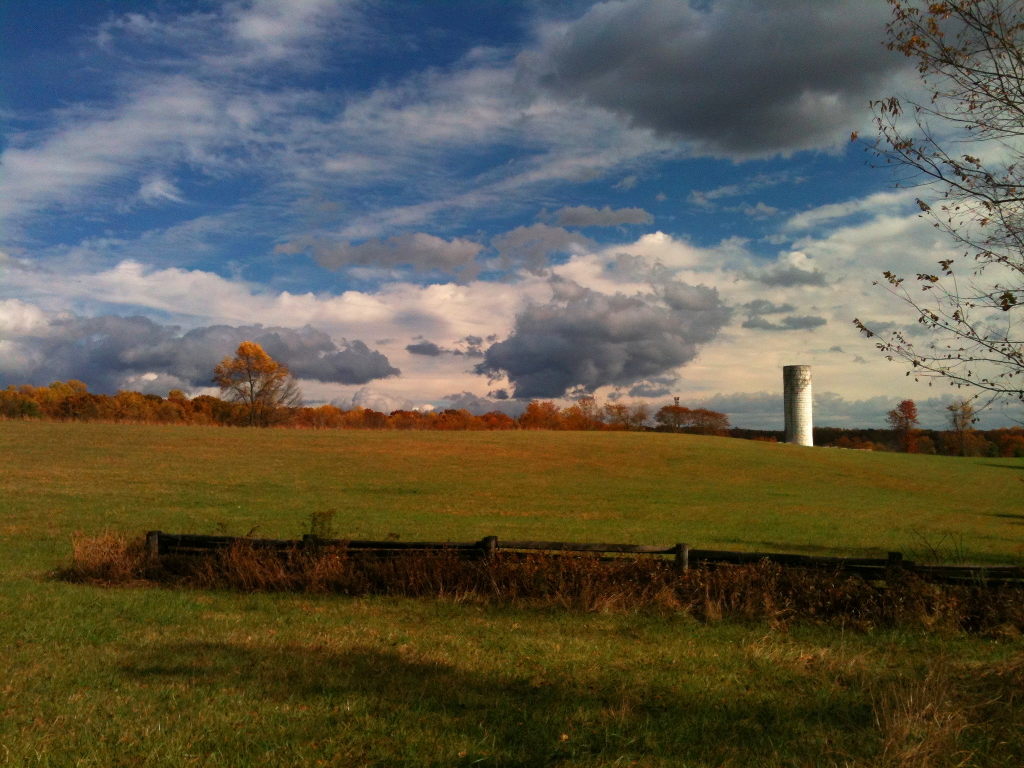 Panoramic photograph of the silo, fields, brick wall, and white and gray clouds set against a bright blue sky